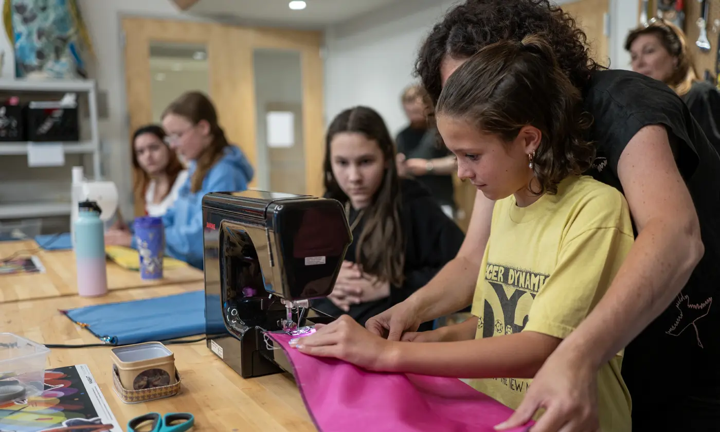 Woman assisting child using sewing machine in class