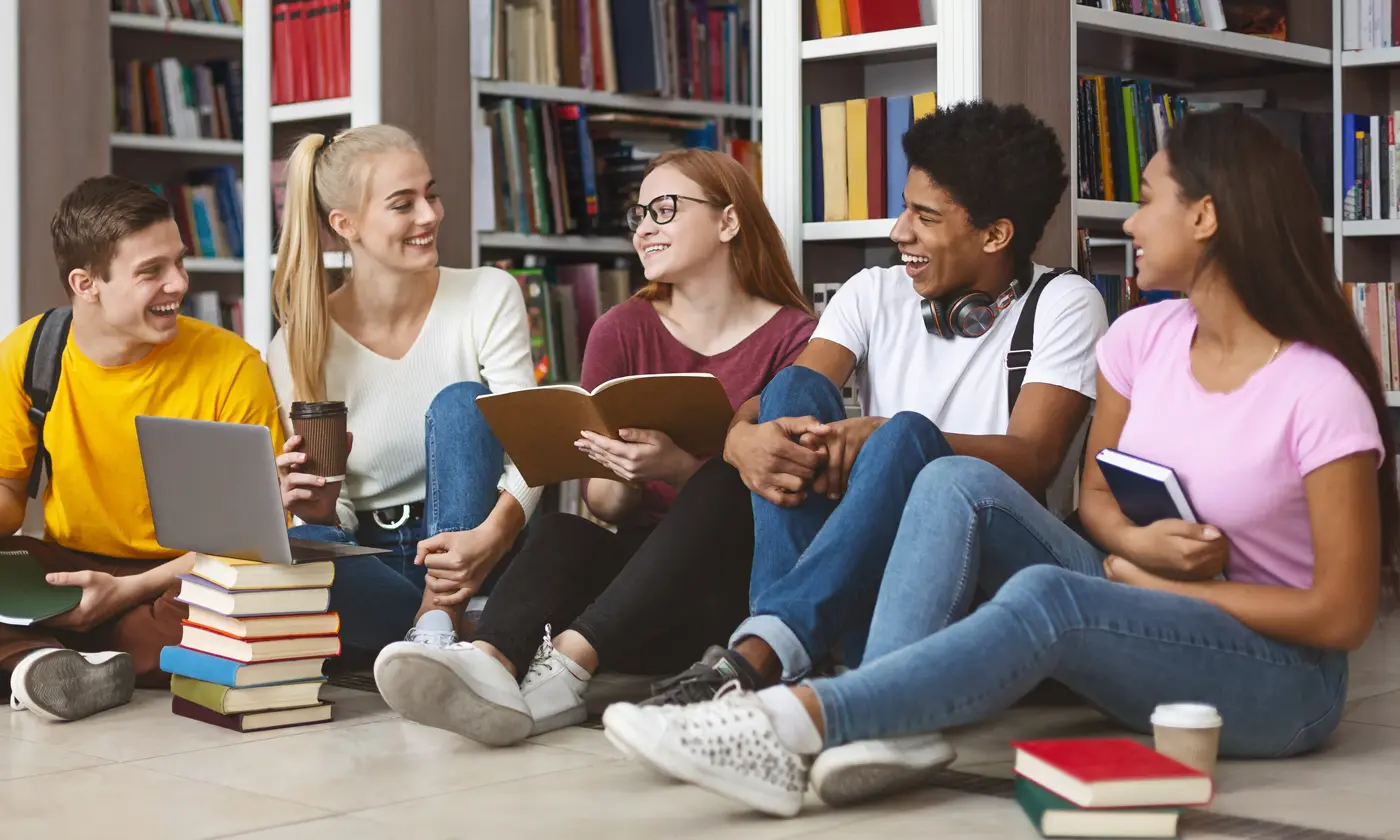 Group of young adults seated on floor in library talking in library surrounded by books